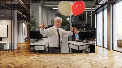 Portrait of a cheerful mature business man holding balloons in the office. Wall mural