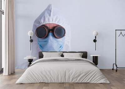 Portrait of a woman in a protective suit wearing a mask with glasses on a white background. A female doctor in uniform during a pandemic. Wall mural