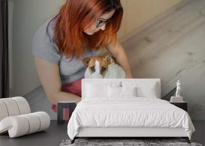 Puppy Jack Russell Terrier is sitting on the lap of his mistress. A woman sits on the floor in her apartment and studies on a laptop. Remote work in quarantine. Wall mural