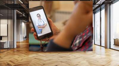 Rear view of an elderly faceless woman talking to a doctor via video chat. Portrait of a doctor on a mobile screen. Online medicine. Bed rest during quarantine. Wall mural