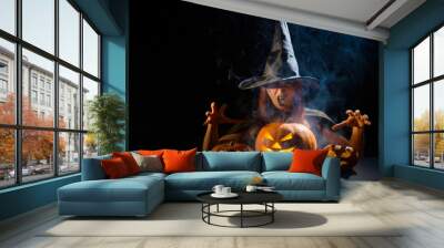 The evil witch casts a spell on pumpkins. Portrait of a woman in a carnival halloween costume in the dark Wall mural