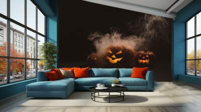 Three creepy halloween steaming pumpkins with a carved luminous smirk on a black background. A handmade jack-o-lantern head with a candle inside in the dark among the fog. Trick or treat. Postcard. Wall mural