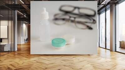 Two pairs of glasses lenses and contact drops in the eyes on a white table.  Wall mural