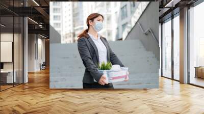 Unhappy woman in a mask is walking along the street with a box of personal stuff on the background of the stairs. A female office employee was fired. Economic crisis during epidemic covid 19. Wall mural