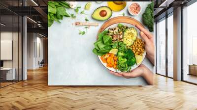 Girl holding plate with hands vegan breakfast. meal in bowl with avocado, mushrooms, broccoli, spinach, chickpeas, pumpkin. top view Wall mural