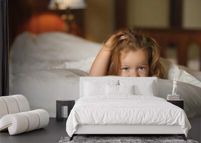 little cute girl 3 years old with dark hair lies in bed with a sad look Wall mural