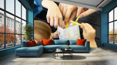 Teenagers take French fries from their younger sister. The family is having lunch at a fast food cafe. The family eats French fries together. Friends Eat French Fries. Photo of people sharing potatoes Wall mural