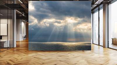 The sun breaks through the clouds illuminating the sea with its rays.  Wall mural