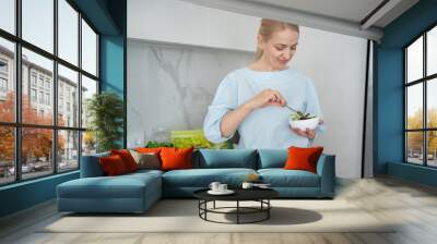 A woman is happily enjoying a fresh salad in a modern kitchen filled with healthy ingredients Wall mural