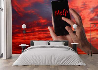 Smartphone in a female hand with a signal for help on a background of dramatic stormy sky Wall mural