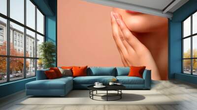 Graceful female fingers touch the face, delicate skin of an even color on an isolated beige background. Wall mural