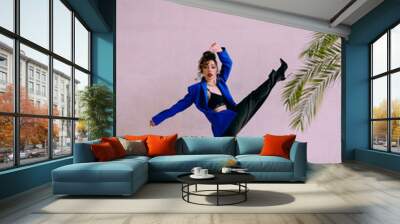 A beautiful glamorous girl with a slim figure in sunglasses in a blue jacket and green at a trendy hot stylish fashion photo shoot posing in a photo studio. Wall mural