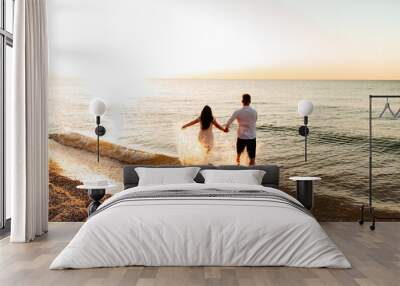 Loving couple in white clothes during a honeymoon at sea walk on the sand at a photoshoot Love Story, ocean coast, beach Wall mural