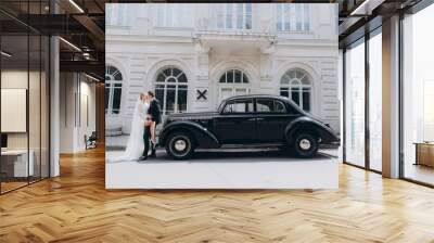 Wedding of a beautiful, stylish couple, a bride in a white wedding dress and a groom in a black suit, tuxedo, in a black retro car. Wall mural