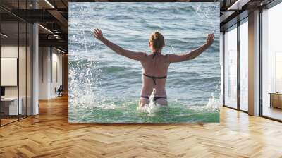 Summer lifestyle portrait of pretty young girl having fun on a tropical beach, splashing sea water Wall mural