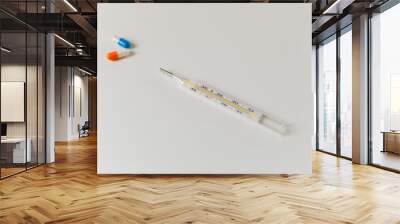 Thermometer and two capsules of orange and blue on a white table Wall mural