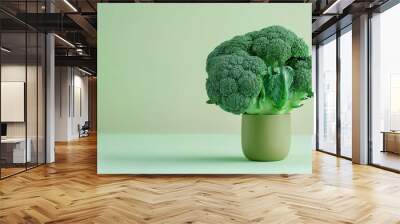 A green broccoli plant stands in a small pot on a green table. Wall mural