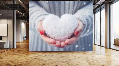 A girl with a red manicure in a gray warm sweater holds a fluffy white heart, close-up, falling snowflakes Wall mural