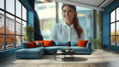 Successful Business Interaction in a Modern Office: A professional woman, wearing a white blouse and blue skirt, smiles as she shakes hands with a business partner in a well-lit, m Wall mural