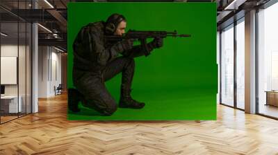 soldier in the studio on a green background with colored light. a man in military uniform with a gun, rifle or machine gun. military. airball player Wall mural