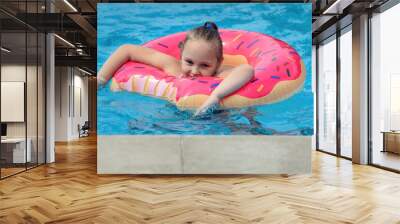 family vacation in summer in an outdoor pool with cool blue water, a girl of eight years old swims on a bright inflatable ring in the pool Wall mural