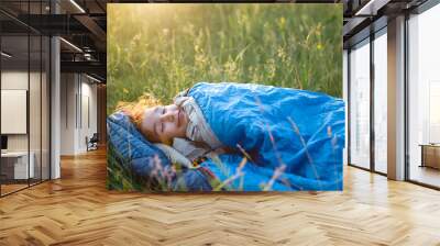 A child sleeps in a sleeping bag on the grass in a camping trip - eco-friendly outdoor recreation, healthy lifestyle, summer time. Sweet and peaceful sleep. Mosquito bites, repellent. Wall mural