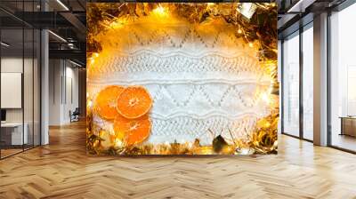 Festive frame made of gold garland with lights and tinsel, slices of dried oranges on a white knitted with a pattern background, copyspace. New year, Christmas, autumn and winter warming atmosphere. Wall mural