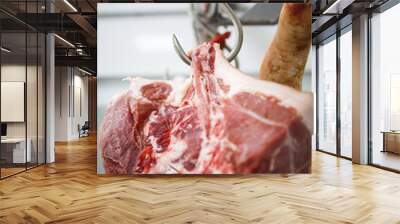 The process of cutting and chopping meat. A man in gloves with an axe and a saw cuts the meat on a special wooden table, pieces of raw meat hanging on hooks Wall mural