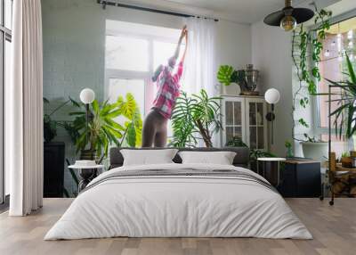 Woman hangs transparent tulle curtains on large windows in the house inside the interior. Spring cleaning, tidying up Wall mural