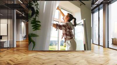 Woman manually washes the window of the house with a rag with spray cleaner and mop inside the interior with white curtains. Restoring order and cleanliness in the spring, cleaning servise Wall mural