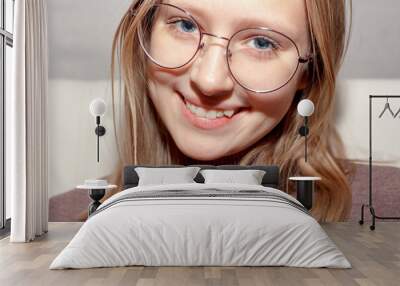 Portrait of a young teenage girl with glasses. Girl smiles and shows crooked growing teeth. You need to go to the dentist to install braces. Wall mural