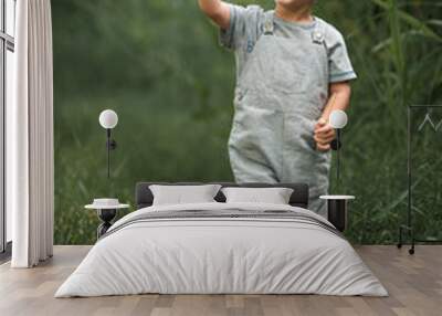 a blond boy in a gray t-shirt and gray overalls walks in the park Wall mural