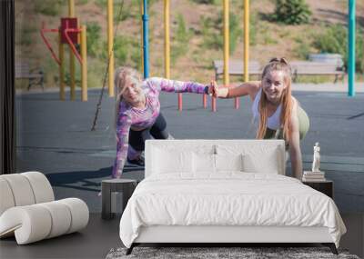 Two beautiful, young and athletic girls doing push-ups on a street playground Wall mural