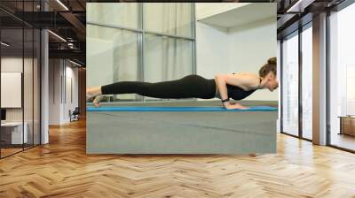 young female doing pilates exercises on blue sport mat in the gym Wall mural