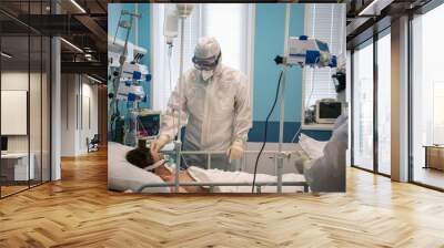 A doctor in a protective suit puts a respiratory mask on a patient with a coronavirus infection covid-19, who is in the intensive care unit of a modern hospital. Wall mural