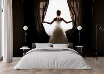 the bride in a wedding dress with a train opens the curtains of the window, stands back, you can see her silhouette, against the light Wall mural