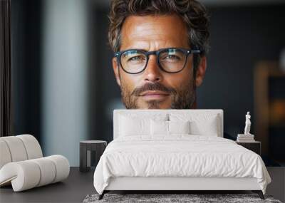 A confident man with glasses poses indoors, showcasing a stylish appearance and a thoughtful expression in a modern setting Wall mural