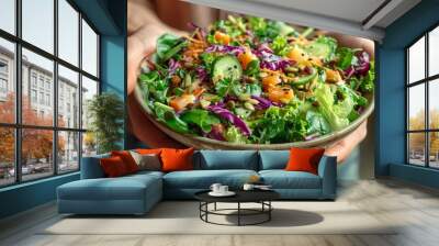 Fresh salad with mixed greens, vegetables, and seeds held by a person indoors during daylight Wall mural