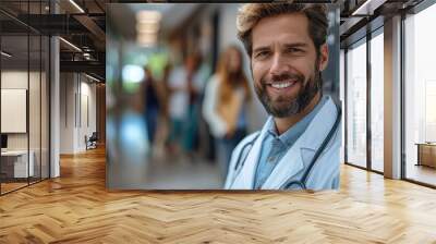 Smiling doctor poses confidently in a hospital corridor while patients walk in the background during a busy daytime shift Wall mural