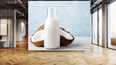 Health content, coconut milk in a glass bottle, coconut halves, light wooden table, close-up, Wall mural