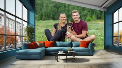 Beautiful romantic couple having fun with a Basenji dog outdoors. Sitting on the green grass Wall mural