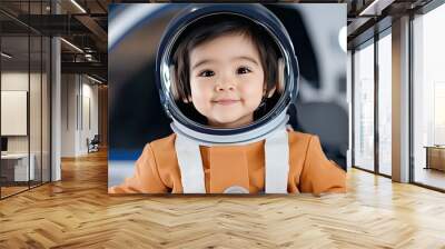 A baby boy dressed in an orange spacesuit gazes with curiosity from the front seat of a spaceship, surrounded by high-tech equipment and warm, inviting lighting Wall mural