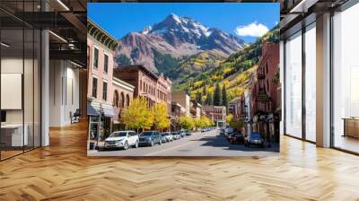 A picturesque street in Telluride, Colorado is lined with trees displaying vibrant autumn colors, while cars are parked along both sides and mountains rise in the background Wall mural