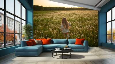 A girl with long hair is running through a field of dandelions. Image with selective focus. Wall mural