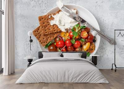 Tasty breakfast or lunch. Salad of colorful cherry tomatoes, onions, herbs, and olive oil, served with crispbread and cream cheese on a gray background top view. Wall mural