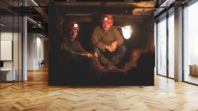 Two young guys in a working uniform and protective helmets, sitting in a low tunnel. Workers of the mine. Miners Wall mural