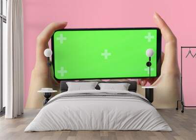 close-up of female hands holding smartphone with blank green screen showing copy space for app or website design, on pink, mockup. Wall mural