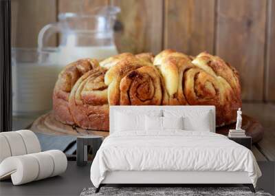 Beautiful yeast cake with cinnamon on a wooden platter close-up, a jug of milk and a glass of milk in the background Wall mural