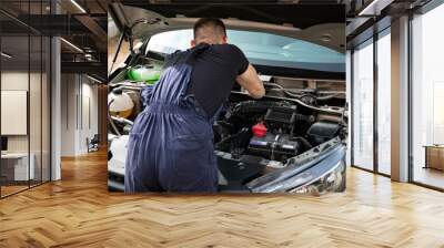 a man repairs a car. a man in blue special clothes to repair the car. engine parts machine repair maintenance breakage problem hands people man master Wall mural