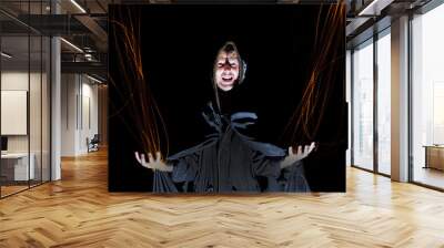 a sorcerer in a black cloak throws fire from his hands on a black background Halloween concept Wall mural